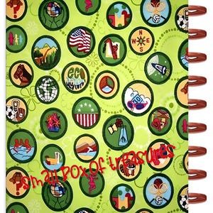Puede incluir: Un cuaderno con espiral con una cubierta verde claro adornada con numerosos parches circulares. Los parches presentan varios dise&ntilde;os, incluyendo un globo terr&aacute;queo, una bandera estadounidense y un caballo. Las palabras "small box of treasures" est&aacute;n escritas en cursiva roja.