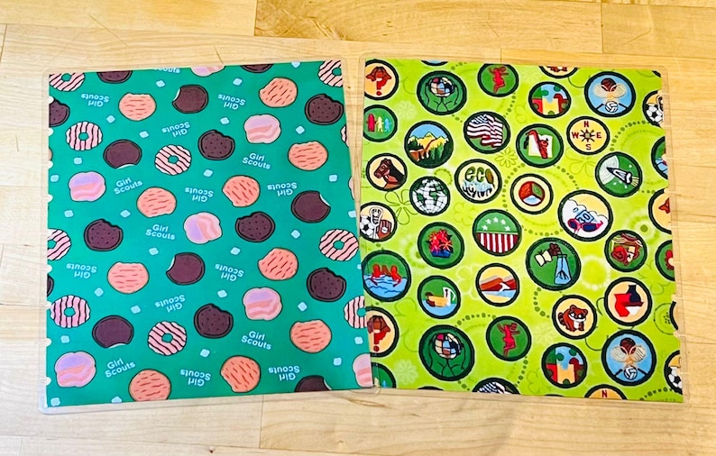 Puede incluir: Dos cuadrados de tela con patrones &uacute;nicos. Uno es verde azulado con ilustraciones de galletas y donuts, y las palabras "Girl Scouts". El otro es verde lima con ilustraciones circulares de varias insignias y la palabra "eco".