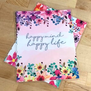 Puede incluir: Varios insertos de planificador con dise&ntilde;os florales. El inserto superior tiene el texto "happy mind happy life" en escritura gris, sobre un fondo rosa y blanco. Los insertos est&aacute;n decorados con flores de acuarela en tonos rosas, morados y azules.