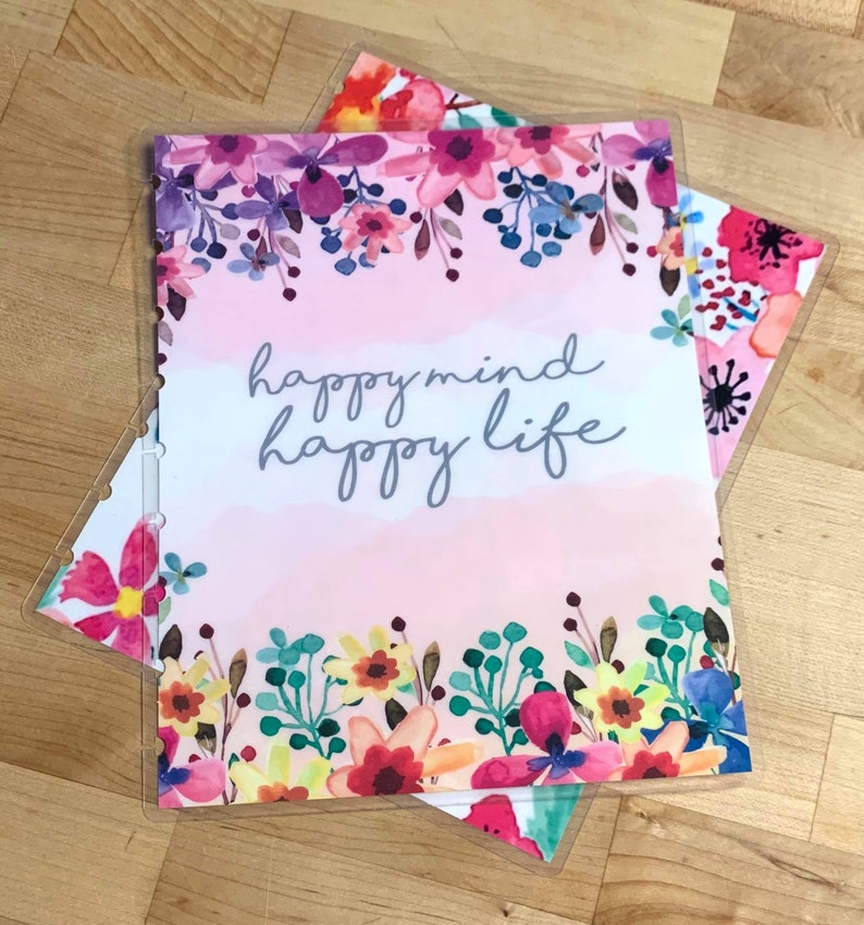 Puede incluir: Varios insertos de planificador con dise&ntilde;os florales. El inserto superior tiene el texto "happy mind happy life" en escritura gris, sobre un fondo rosa y blanco. Los insertos est&aacute;n decorados con flores de acuarela en tonos rosas, morados y azules.