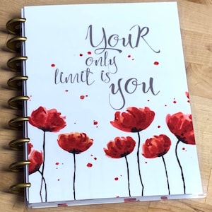 May include: A white planner with a gold coil binding and a motivational quote that reads "Your only limit is you". The cover features a watercolor design of red poppies with a white background.