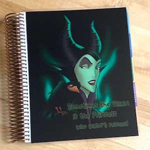Puede incluir: Una agenda negra con una imagen verde y negra de Mal&eacute;fica de La Bella Durmiente. El texto "Sometimes the Villain is the Princess who wasn't rescued" est&aacute; impreso en la portada.