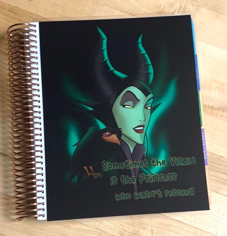 Puede incluir: Una agenda negra con una imagen verde y negra de Mal&eacute;fica de La Bella Durmiente. El texto "Sometimes the Villain is the Princess who wasn't rescued" est&aacute; impreso en la portada.