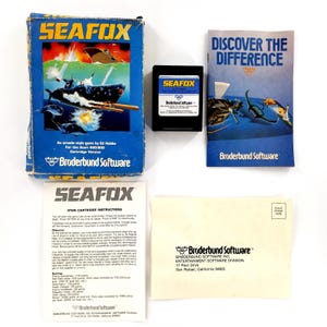 Könnte beinhalten: Ein Vintage-SEAFOX-Videospielset für Atari 400/800. Das Box-Art zeigt eine U-Boot-Szene mit dem Spieltitel in fetten gelben Buchstaben. Enthält die Spielkassette, die Bedienungsanleitung und Werbematerialien. Das Spiel ist von Broderbund Software.
