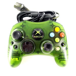 May include: A translucent green video game controller with a black wired cable and connector. The device features a central Xbox logo button, two black analog sticks, a black directional pad, and four colored action buttons labeled A, B, X, and Y.