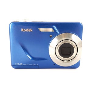 Puede incluir: Una cámara digital Kodak de color azul metálico con la etiqueta 10.2 megapixels en la parte frontal. El objetivo plateado tiene el texto Kodak AF 3x Optical Aspheric Lens 32mm-96mm Equivalent. Un pequeño flash se sitúa sobre el objetivo.