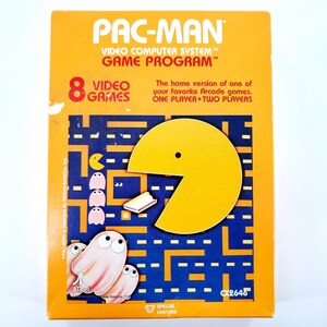 May include: A vintage Pac-Man video game cartridge box. The box is orange with the Pac-Man logo and game details. The game features a yellow Pac-Man character, ghosts, and a maze design. The box reads "8 Video Games" and "Video Computer System Game Program".
