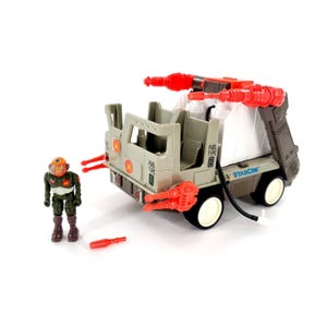 Könnte beinhalten: Ein Vintage-Starcom-Spielzeugset mit einem grauen Militär-Truck mit roten Raketenwerfern und einer passenden Actionfigur. Der Truck hat weiße Räder und den Text "FUEL TYPE" und "STARCOM". Ein rotes Zubehör liegt am Boden.