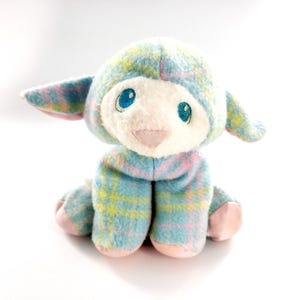 May include: A plush lamb toy with a blue, yellow, and pink plaid pattern. The lamb has a white face with blue embroidered eyes and a pink nose. The ears and feet are pink.