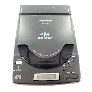 May include: A black Panasonic KXL-D740 portable CD-ROM player featuring a 4X speed label, a top-loading disc compartment, a small LCD screen, and physical control buttons labeled OPEN, LOCK, and play/pause/charge symbols on the front panel.