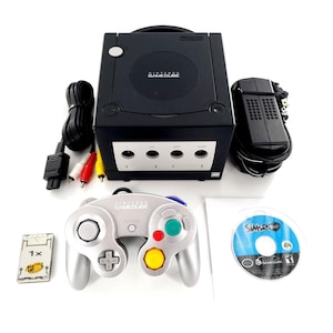 May include: A black Nintendo GameCube console with a silver controller, a power adapter, an AV cable, a memory card, and a The Sims 2 Pets game disc. The console features four controller ports on the front and the Nintendo GameCube logo on top.