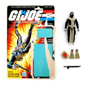 May include: A vintage G.I. Joe action figure set. The packaging features a diver graphic with the text "G.I. Joe: A Real American Hero." The set includes a diver figure, accessories, and a harpoon rifle. The packaging is slightly damaged.