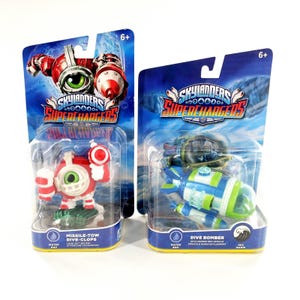 May include: Two Skylanders SuperChargers toys in their original packaging. One is a red and white robot named Missile-Tow Dive-Clops. The other is a blue, green, and white submarine called Dive Bomber. Both toys are for ages 6+.