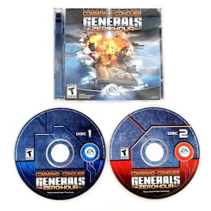 May include: A Command & Conquer Generals Zero Hour expansion pack PC game case featuring an aircraft carrier explosion on the cover, accompanied by two circular game discs labeled Disc 1 in blue and Disc 2 in red, each with the EA Games logo.