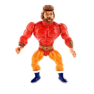 Puede incluir: Figura de acción vintage de un hombre musculoso con torso y brazos rojos, piernas naranjas y botas azules. La figura tiene barba, pelo y diadema marrones, y un cinturón dorado.