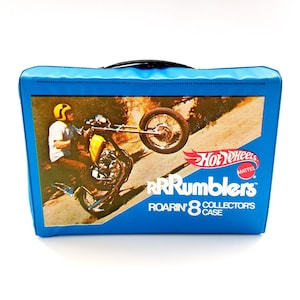 May include: A blue Hot Wheels RRRumblers Roarin' 8 Collector's Case. The case features a graphic of a motorcycle doing a wheelie. The Hot Wheels logo is in red and white. The case has a black handle.