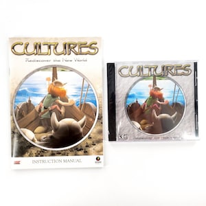 Puede incluir: La imagen muestra un juego para PC titulado "Cultures: Rediscover the New World". Se muestran el manual de instrucciones y la caja del CD del juego. La portada presenta un personaje de dibujos animados vikingo en un barco. El manual de instrucciones dice "Instruction Manual."