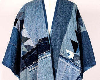 May include: A denim kimono made from patchwork pieces of blue jeans. The kimono has a V-neck and is open in the front. The kimono is made from a variety of different shades of blue denim.