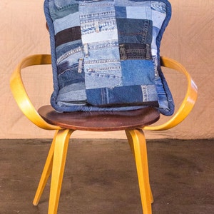 May include: A yellow wooden chair with a brown seat and a blue denim patchwork pillow on top.