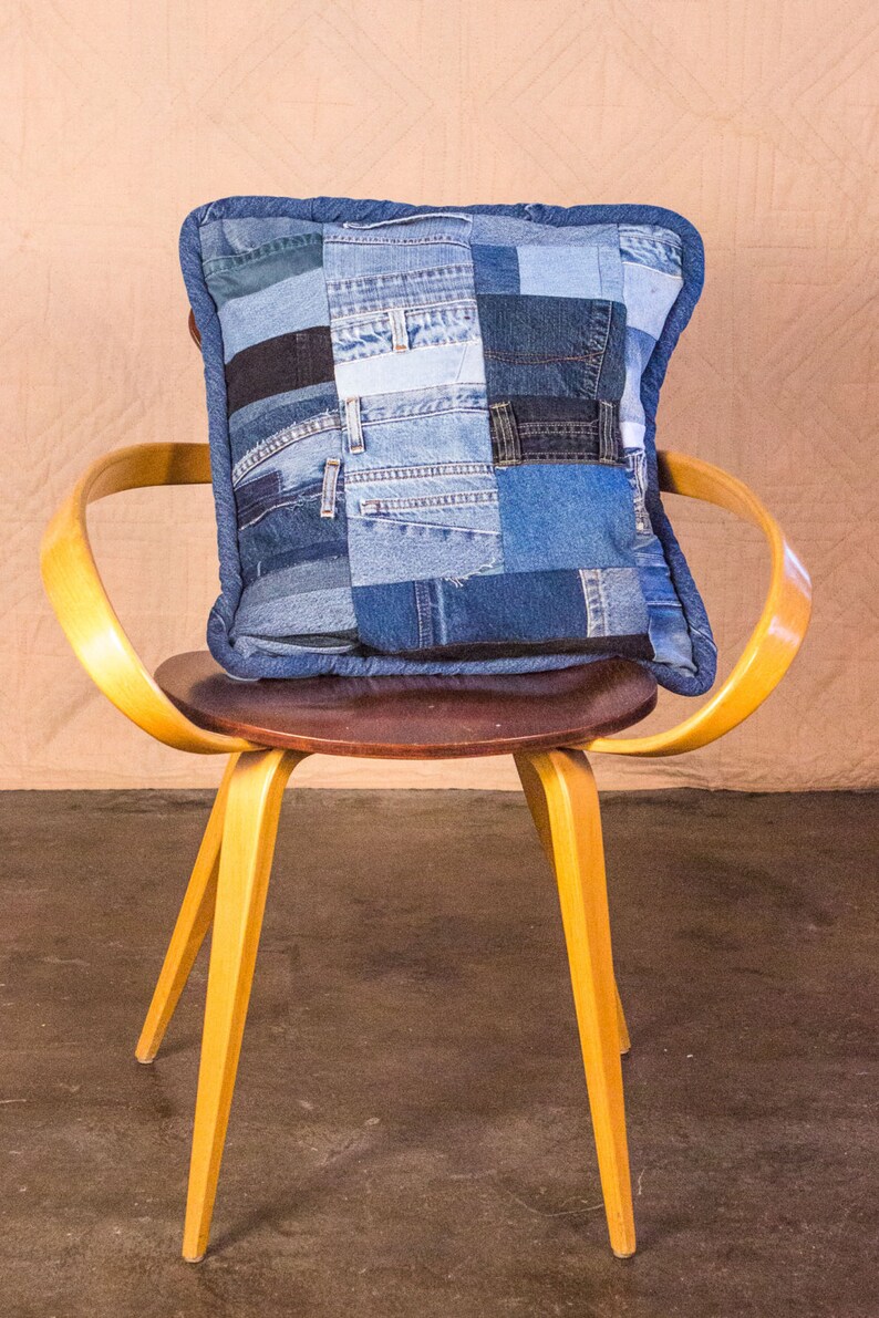May include: A yellow wooden chair with a brown seat and a blue denim patchwork pillow on top.