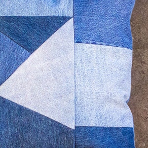 May include: A blue denim pillow with a geometric pattern. The pillow is made from different shades of blue denim and has a white triangle in the center.