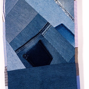 May include: A patchwork quilt made from different shades of blue denim fabric. The quilt is made up of various sized squares and rectangles, with a pocket sewn into one of the squares. The quilt is edged with a variety of patterned fabrics, including plaid, striped, and solid colors.