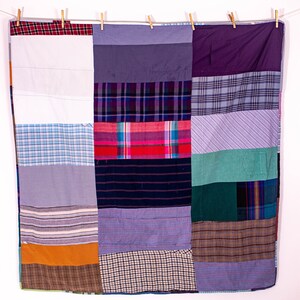 May include: A patchwork quilt made from repurposed fabric scraps. The quilt is made up of squares of different colors and patterns, including plaid, striped, and solid colors. The quilt is hanging on a clothesline.