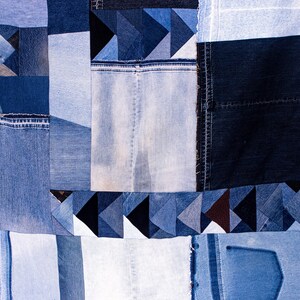 May include: A patchwork quilt made from denim fabric in various shades of blue. The quilt is made up of squares and triangles, and some of the pieces have visible seams. The quilt is a unique and handmade piece of art.