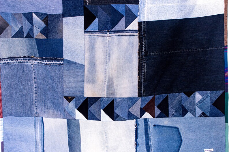 May include: A patchwork quilt made from denim fabric in various shades of blue. The quilt is made up of squares and triangles, and some of the pieces have visible seams. The quilt is a unique and handmade piece of art.