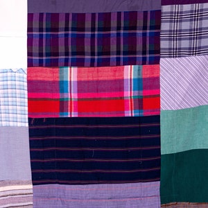 May include: A patchwork quilt made from different fabrics in various shades of purple, blue, red, green, and brown. The quilt is made up of squares and rectangles of fabric sewn together.