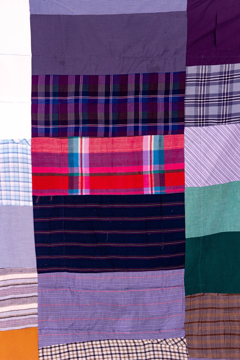 May include: A patchwork quilt made from different fabrics in various shades of purple, blue, red, green, and brown. The quilt is made up of squares and rectangles of fabric sewn together.