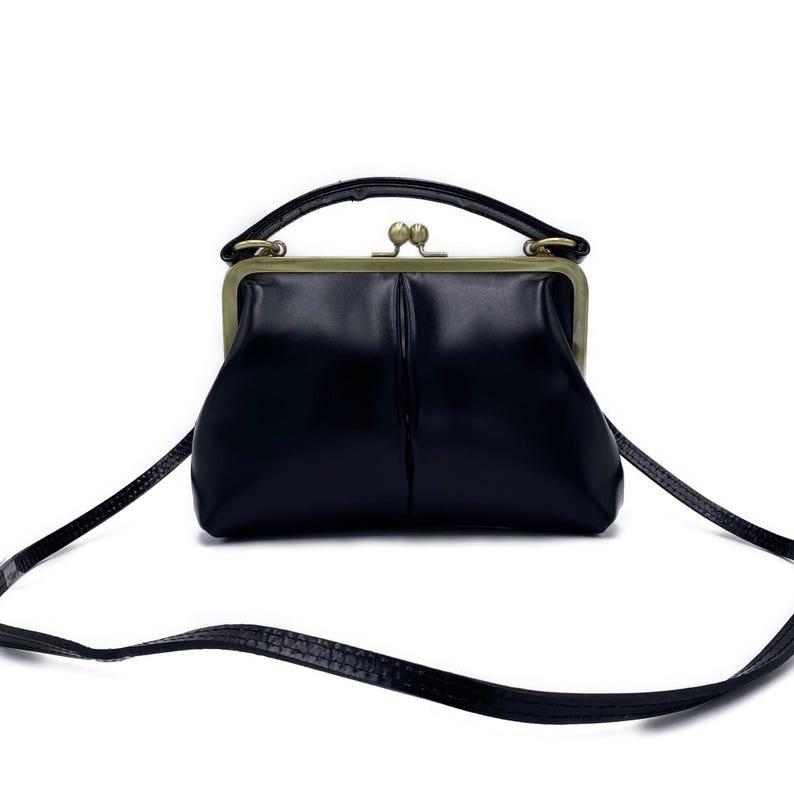 K&ouml;nnte beinhalten: Eine wei&szlig;e Keramik-Tasse mit schwarzem Henkel und dem Text "But First, Coffee" in schwarzer, handschriftlicher Schrift. Die Tasse steht auf einer wei&szlig;en Oberfl&auml;che.