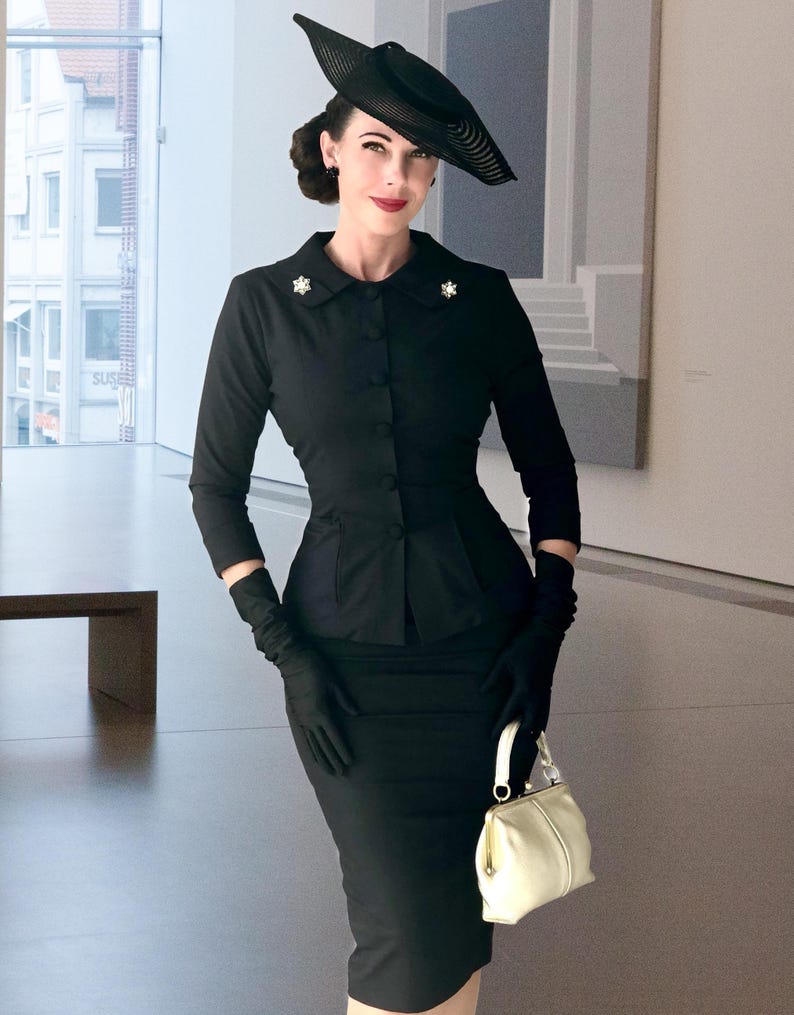 May include: A black long-sleeved jacket with a collar and small star-shaped pins, paired with a matching black pencil skirt. The outfit includes a wide-brimmed black hat, black gloves, and a small cream-colored handbag with a gold-toned clasp.