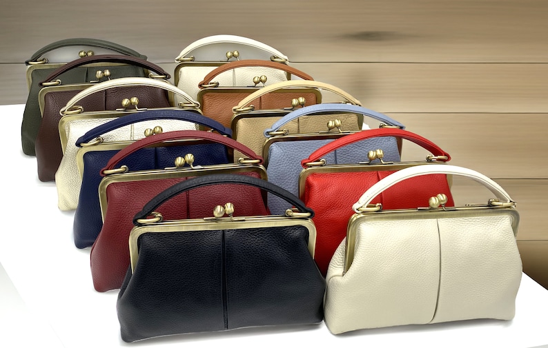 May include: A collection of ten leather handbags in various colors including black, white, red, blue, brown, and olive green. Each bag features a textured surface, a single top handle, and a brass-toned metal kiss-lock frame closure at the top.