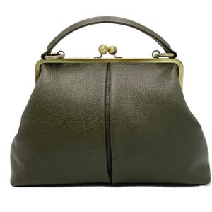 Puede incluir: Un bolso de mano color verde oliva con superficie texturizada, que cuenta con un asa superior y un cierre de marco met&aacute;lico en tono lat&oacute;n con dos pomos esf&eacute;ricos. El bolso tiene una forma estructurada con una costura vertical en el centro.