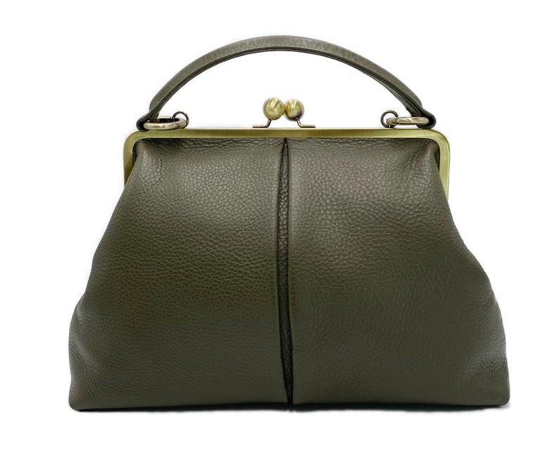 Puede incluir: Un bolso de mano color verde oliva con superficie texturizada, que cuenta con un asa superior y un cierre de marco met&aacute;lico en tono lat&oacute;n con dos pomos esf&eacute;ricos. El bolso tiene una forma estructurada con una costura vertical en el centro.