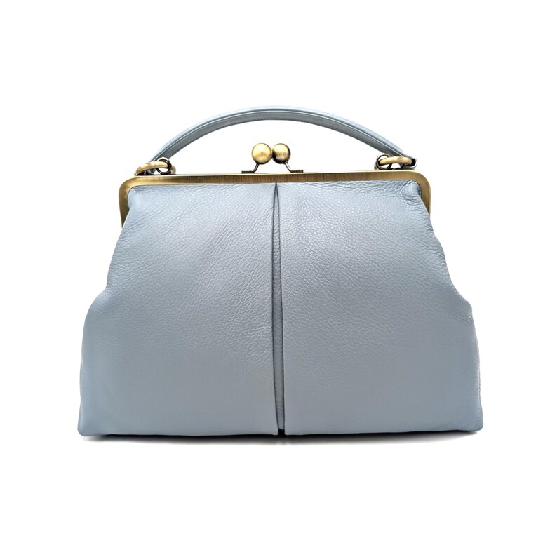 Puede incluir: Un bolso de mano azul claro con superficie texturizada, que presenta un asa superior curva y un cierre de marco de metal en tono lat&oacute;n con dos pomos esf&eacute;ricos. El bolso tiene una forma estructurada con una costura vertical central.