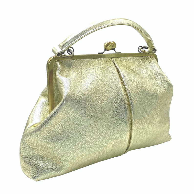 Puede incluir: Un bolso de mano en color dorado met&aacute;lico con una superficie texturizada similar al cuero, que presenta un marco de metal en tono lat&oacute;n, un asa superior &uacute;nica y un mecanismo de cierre de broche central. El bolso tiene un cuerpo suave y flexible.