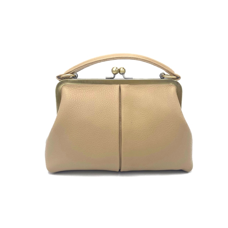 May include: A beige leather handbag with a pebbled texture, featuring a structured brass-toned metal frame, a top handle, and a kiss-lock closure. The bag has a soft, rounded shape with a vertical seam down the center of the front panel.