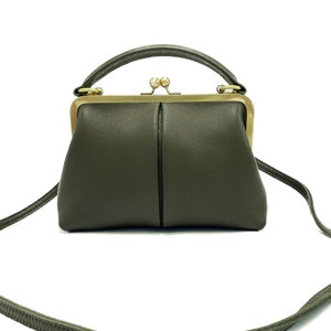 May include: A small, olive green leather handbag with a gold clasp and a top handle. The bag has a long strap that can be used to carry it over the shoulder.