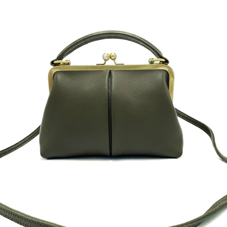 May include: A small, olive green leather handbag with a gold clasp and a top handle. The bag has a long strap that can be used to carry it over the shoulder.