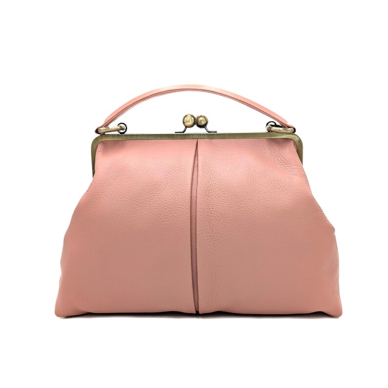 Puede incluir: Un bolso de mano rosa empolvado con superficie texturizada, que cuenta con un asa superior curva y un marco met&aacute;lico en tono lat&oacute;n. El bolso se cierra con un mecanismo de cierre de doble bola en el centro y tiene una forma suave y redondeada.