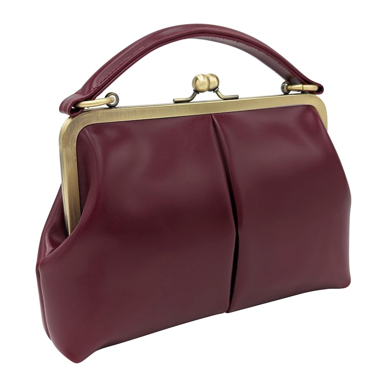 K&ouml;nnte beinhalten: Burgunderfarbene Handtasche mit oberem Griff und Schnallenverschluss. Die Tasche hat einen Vintage-Stil mit strukturierter Form und goldfarbenem Metallrahmen. Der Griff ist gebogen und die Tasche scheint aus Leder oder einem &auml;hnlichen Material zu sein.