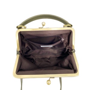 May include: An open green leather purse with a brass clasp and a brown fabric lining. The purse has a small pocket inside.
