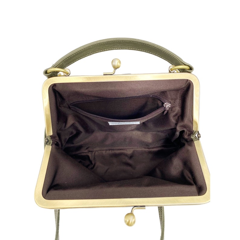 May include: An open green leather purse with a brass clasp and a brown fabric lining. The purse has a small pocket inside.