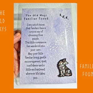 May include: A rectangular card with a light purple watercolour background featuring the text The Old Ways Familiar found and a poem about familiars. A small wolf-shaped enamel pin is attached to the bottom right, with a trail of white stars above.