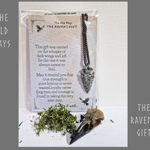 May include: A silver-toned arrowhead pendant on a dark metal chain, packaged with a card titled The Old Ways The Raven's Gift. The card features printed text about strength and loyalty, accompanied by a small bird skull and green moss.