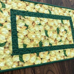 May include: A green and yellow quilted table runner with a lemon print. The runner has a green border with a scalloped edge.