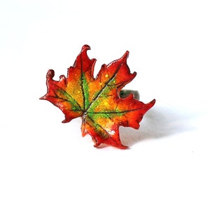 May include: A red, orange, and green maple leaf ring. The leaf is detailed with veins and has a shiny finish.