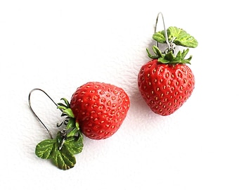 May include: A pair of dangle earrings featuring realistic red strawberry charms with textured green leaves. Each strawberry is attached to a silver-toned metal hook wire, creating a fruit-themed accessory with detailed seeds and vibrant coloring.